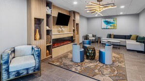A modern living room with a fireplace, comfortable seating, a flat-screen TV, and a contemporary light fixture. - Best Western Plus Savannah Gateway (Savannah)