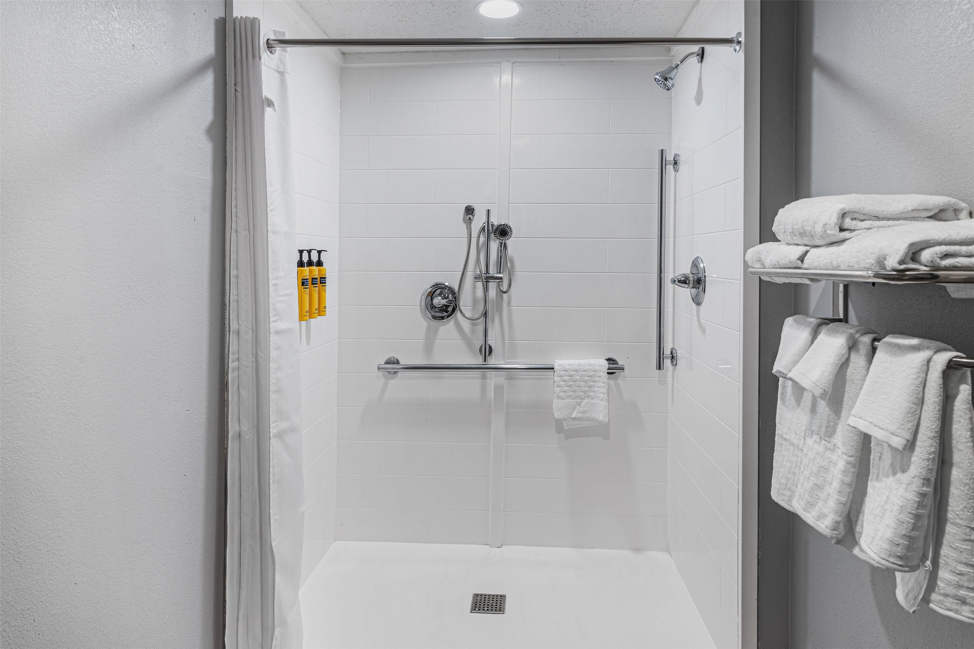 A modern shower area with a glass door, a towel rack with folded towels, and a shelf with toiletries.