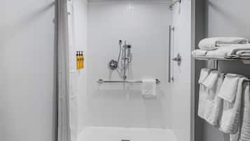 A modern shower area with a glass door, a towel rack with folded towels, and a shelf with toiletries.