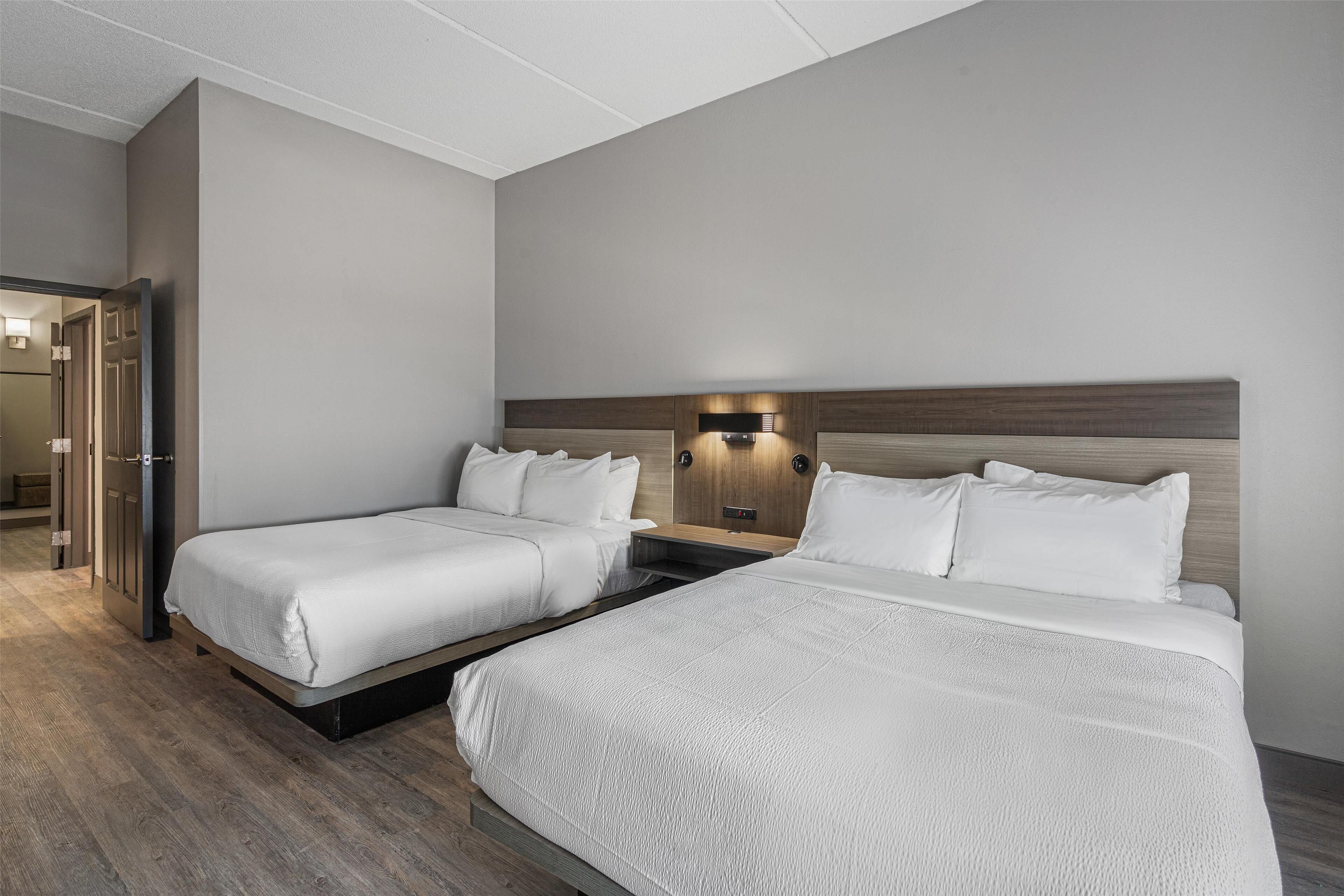 A hotel room with two beds, a wooden headboard, a nightstand, and a wall-mounted light fixture.