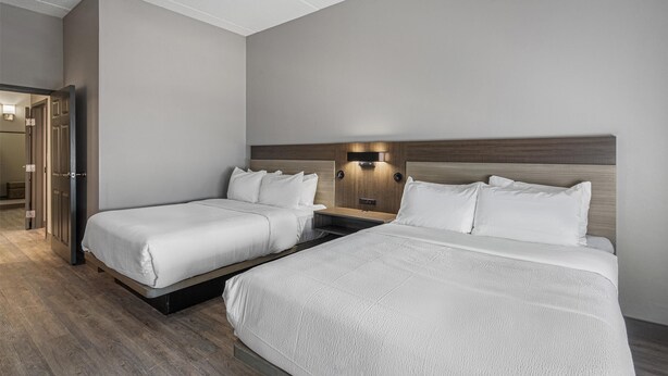 A hotel room with two beds, a wooden headboard, a nightstand, and a wall-mounted light fixture.
