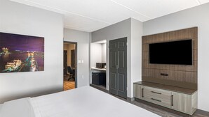 A modern hotel room with a large bed, a flat-screen TV mounted on a wooden panel, a small kitchenette, and a door leading to another room. - Best Western Plus Savannah Gateway (Savannah)
