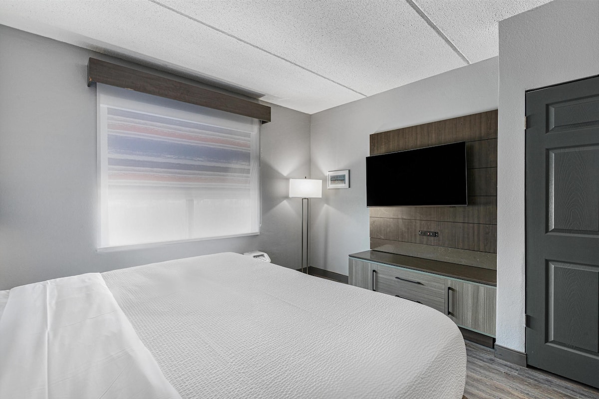A hotel room with a bed, a TV mounted on the wall, a desk with drawers, and a door.