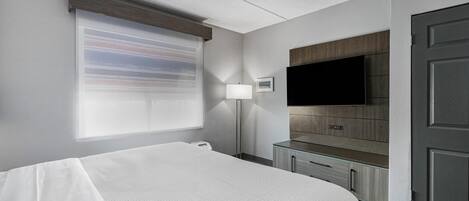 Ett hotellrum med en säng, en tv som är monterad på väggen, ett skrivbord med lådor och en dörr.