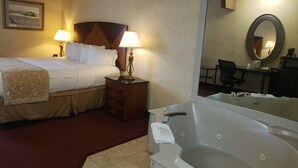 Ein Hotelzimmer mit einem Bett, zwei Nachttischlampen, einem Nachttisch, einem Schreibtisch mit Stuhl, einem großen Spiegel und einer Badewanne.