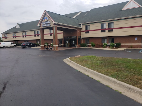Hotel com entrada coberta, estacionamento e área gramada.