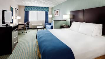 Ein Hotelzimmer mit einem großen Bett, einem Schreibtisch mit Stuhl, einem Fernseher und einem Fenster mit Vorhängen.