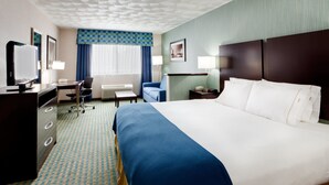 A hotel room with a large bed, a desk with a chair, a television, and a desk lamp.