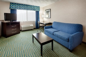 Habitación de hotel con un sofá azul, una mesita, un televisor sobre un aparador, un escritorio y una silla.