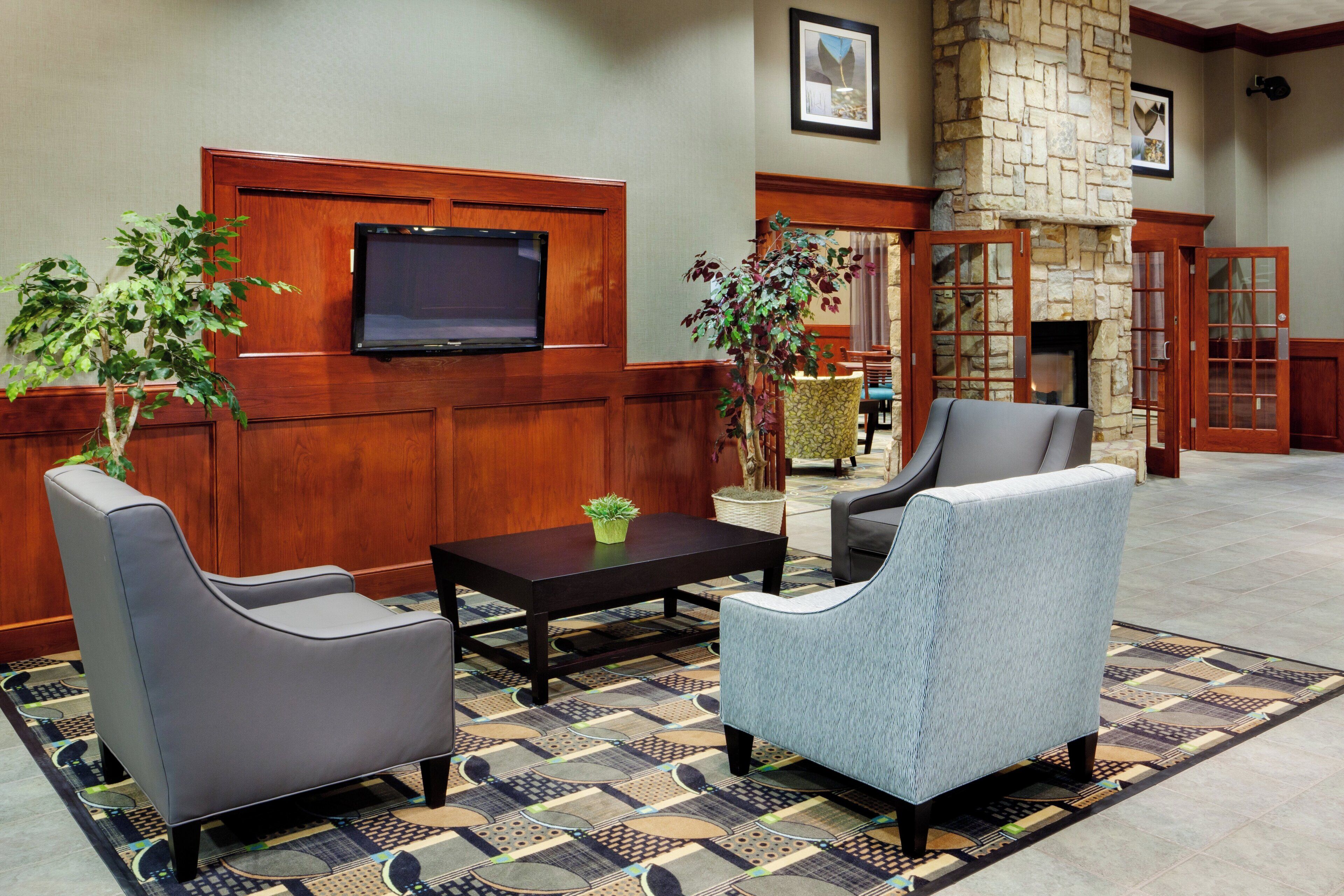 A lobby with a television mounted on the wall, two armchairs, a coffee table, and a patterned rug.