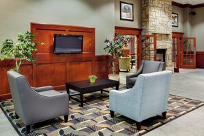 A lobby with a television mounted on the wall, two armchairs, a coffee table, and a patterned rug. - Holiday Inn Express & Suites Smithfield - Providence by IHG (Smithfield)