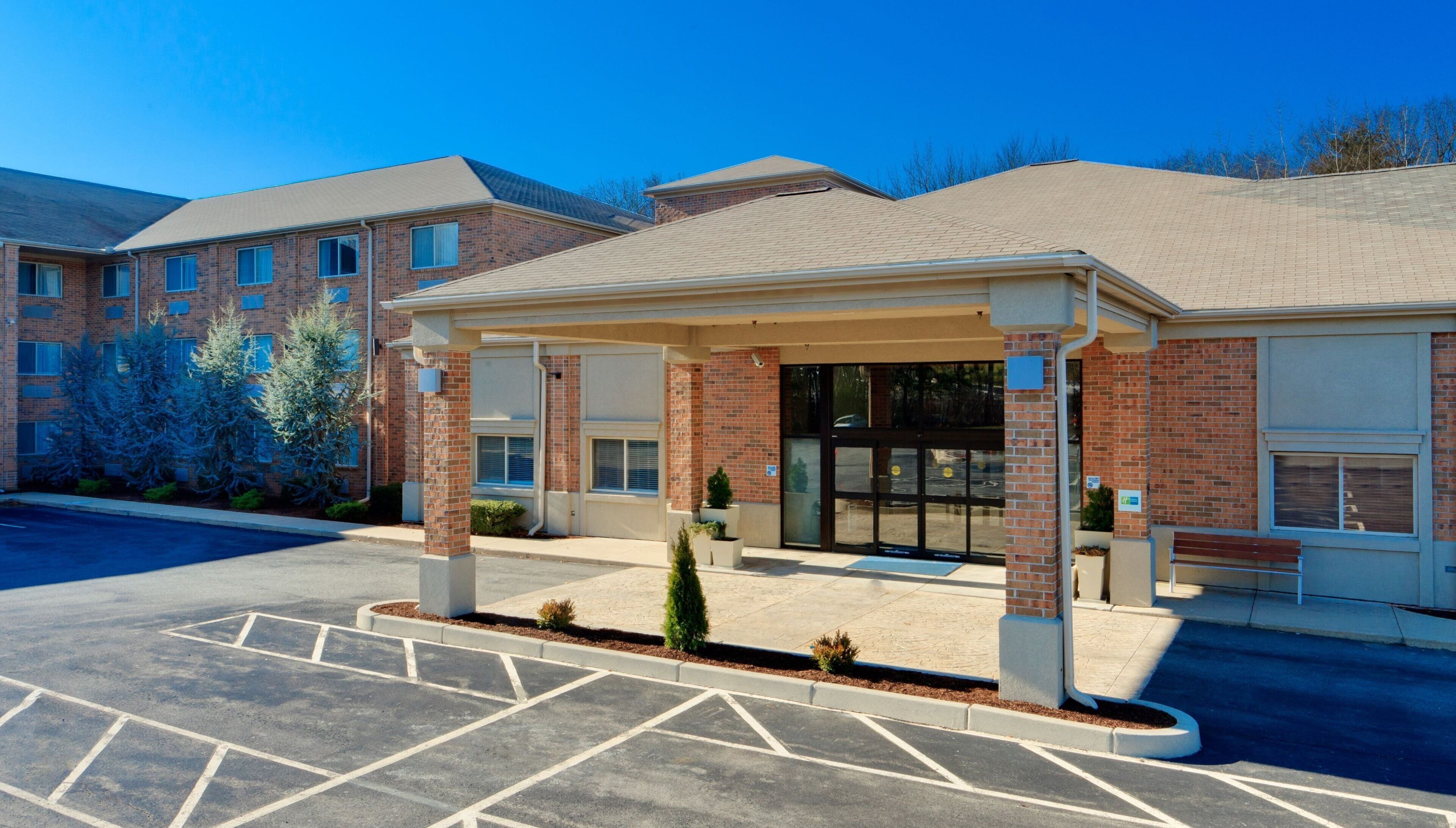 A building with a covered entrance, brick facade, and a parking lot with marked spaces.