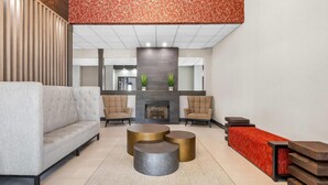 Eine moderne Lobby mit einer Couch, Sesseln, einem Kamin und einer langen roten Wand als Blickfang.