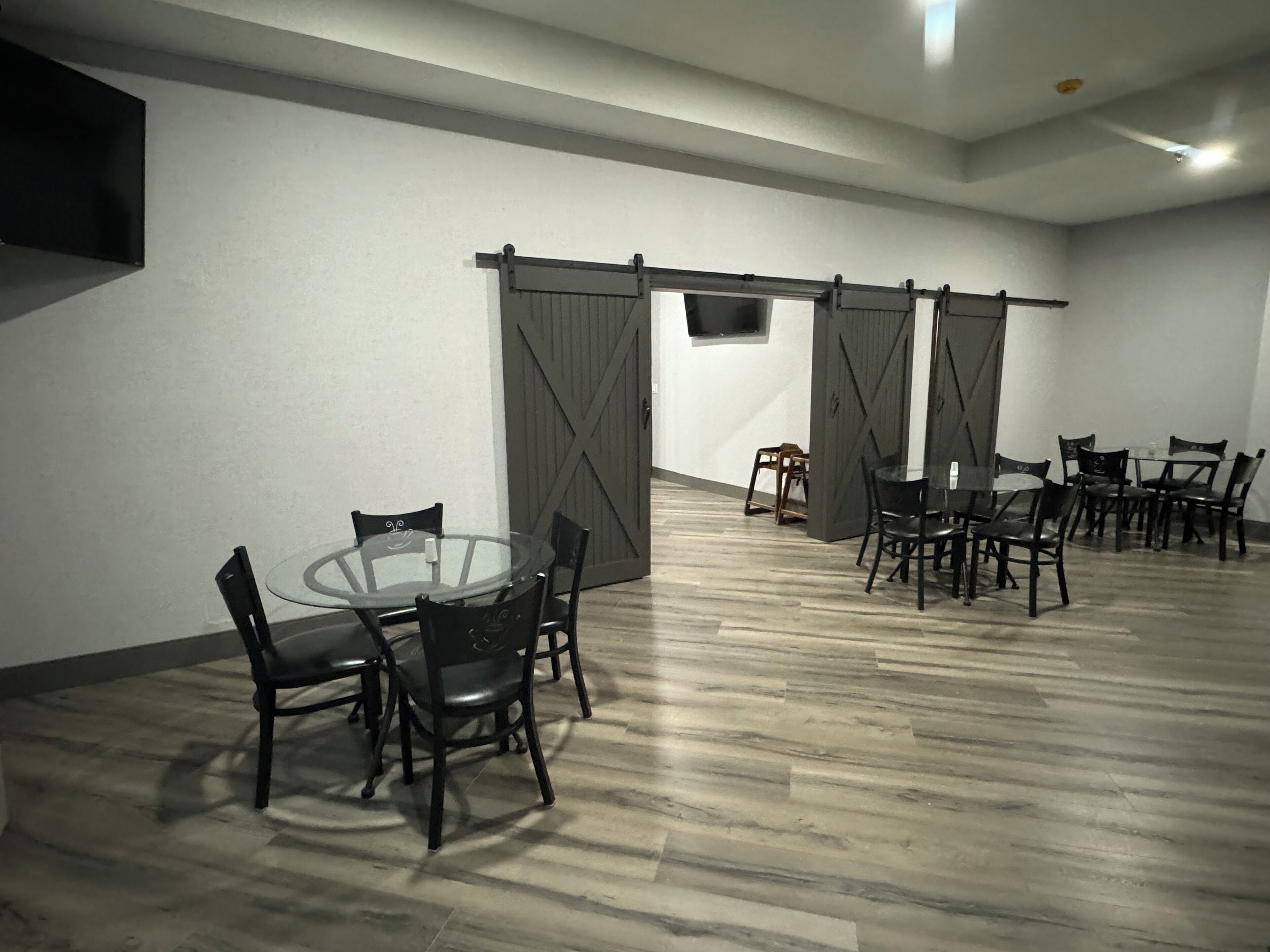 A conference room with a glass table, black chairs, a TV mounted on the wall, and sliding barn doors.