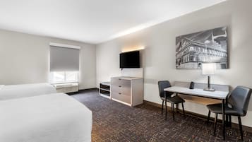 Une chambre d’hôtel avec deux lits, un bureau avec une chaise, un téléviseur à écran plat, une lampe de bureau et un tableau au mur.