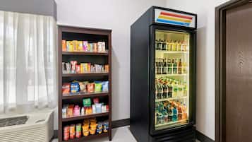 A room with a snack shelf stocked with various packaged foods and a beverage refrigerator containing multiple bottles and cans.
