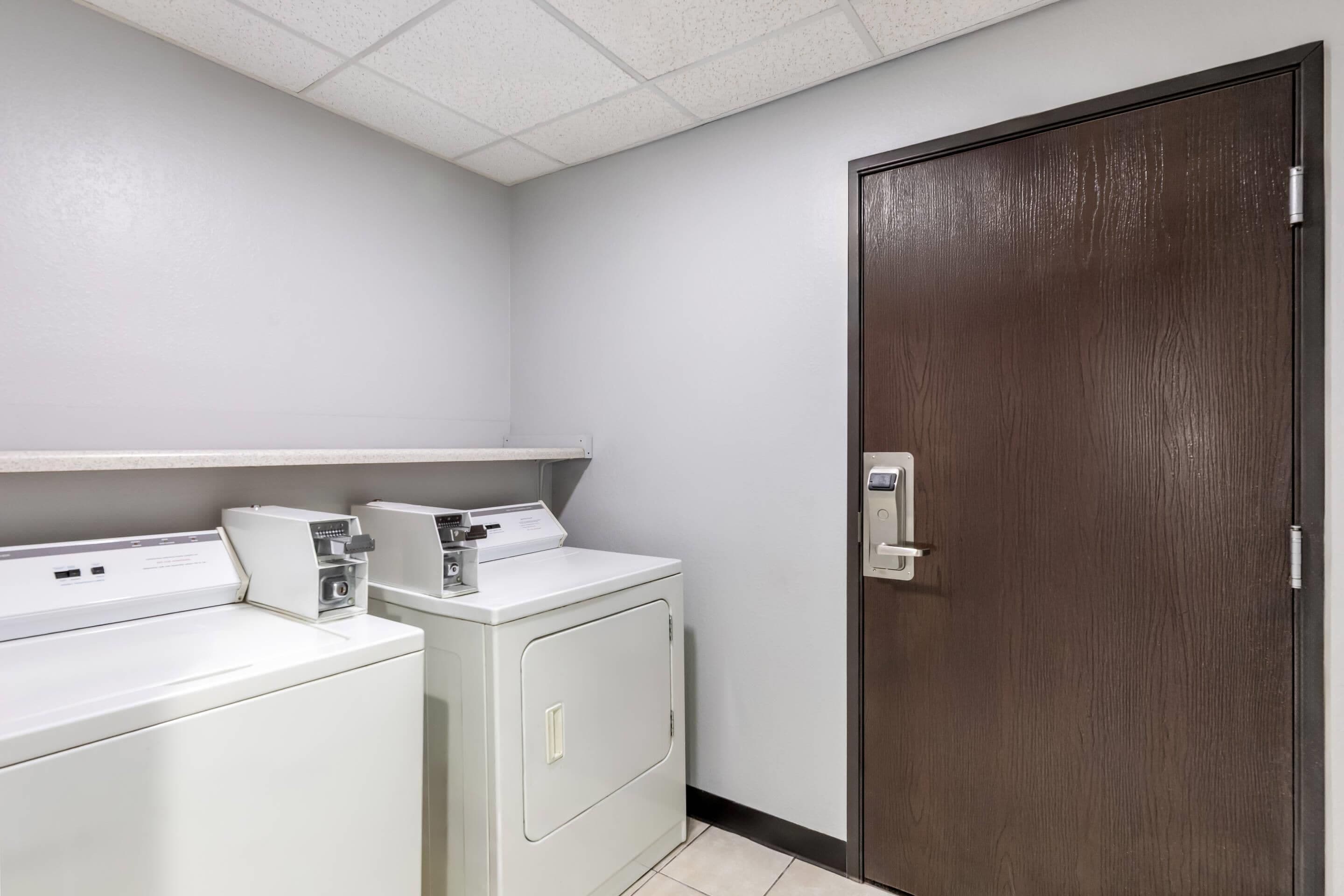 Un lavadero con dos lavadoras y una secadora, una puerta de madera y un techo blanco.