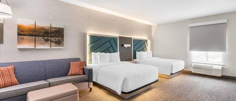 A hotel room with a sofa, two beds, a wall-mounted artwork, and a large window.