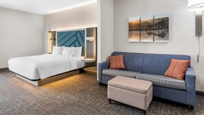 Ein Hotelzimmer mit einem Bett, einer Couch, einem Hocker und einem Wandbild.