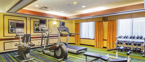 Gimnasio de hotel con equipo de ejercicio, una banca y mancuernas.