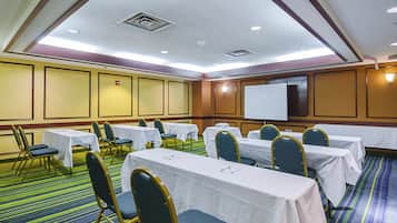 Un salón de conferencias con mesas, sillas, una pantalla de proyector y piso alfombrado.