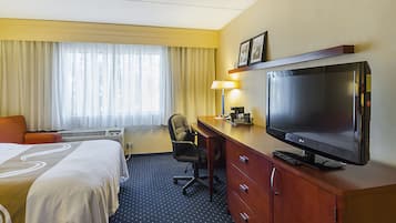 A hotel room with a bed, desk, chair, television, and a window with curtains.
