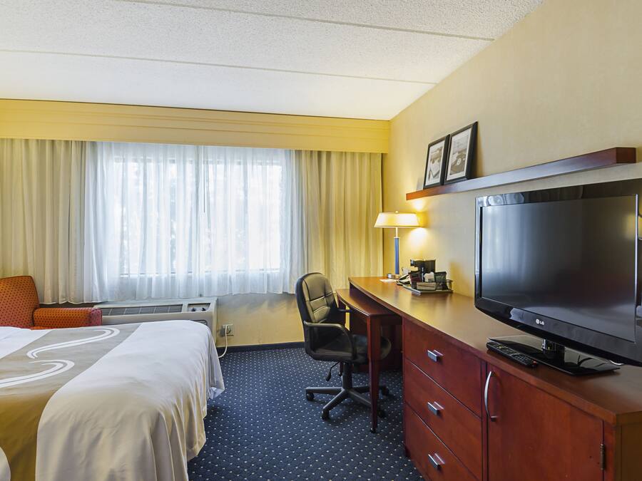 A hotel room with a bed, desk, chair, television, and a window with curtains.