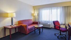 A hotel room with a red sofa, a small table, a red office chair, two lamps, and a large window with curtains. - Quality Inn Boston - Revere (Revere)