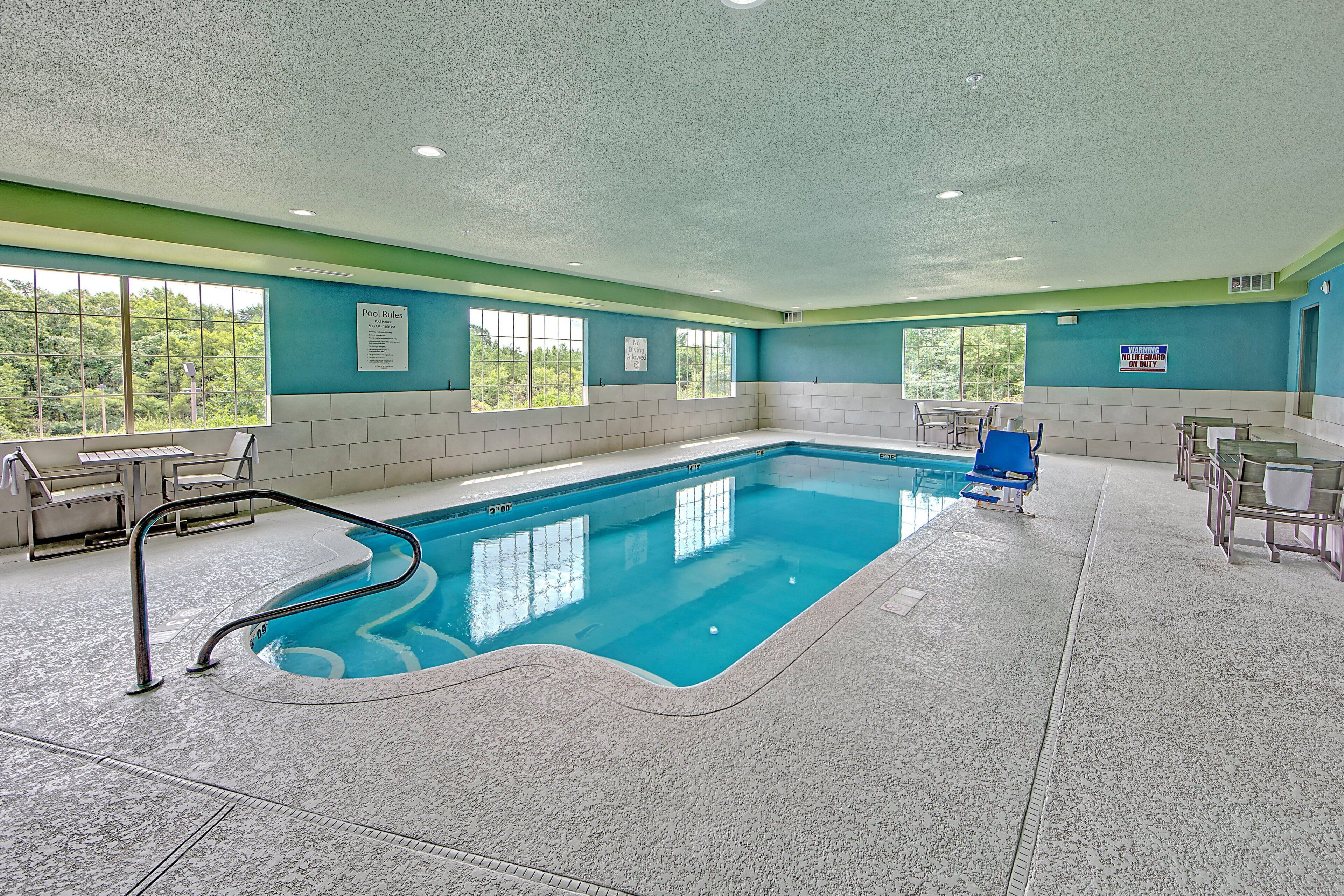 Una piscina interior con normas de seguridad visibles, una silla de socorrista y vistas al exterior a través de grandes ventanales.