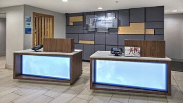 Dos mostradores de recepción con pantallas digitales, un letrero de Holiday Inn Express y un aviso de establecimiento libre de humo.