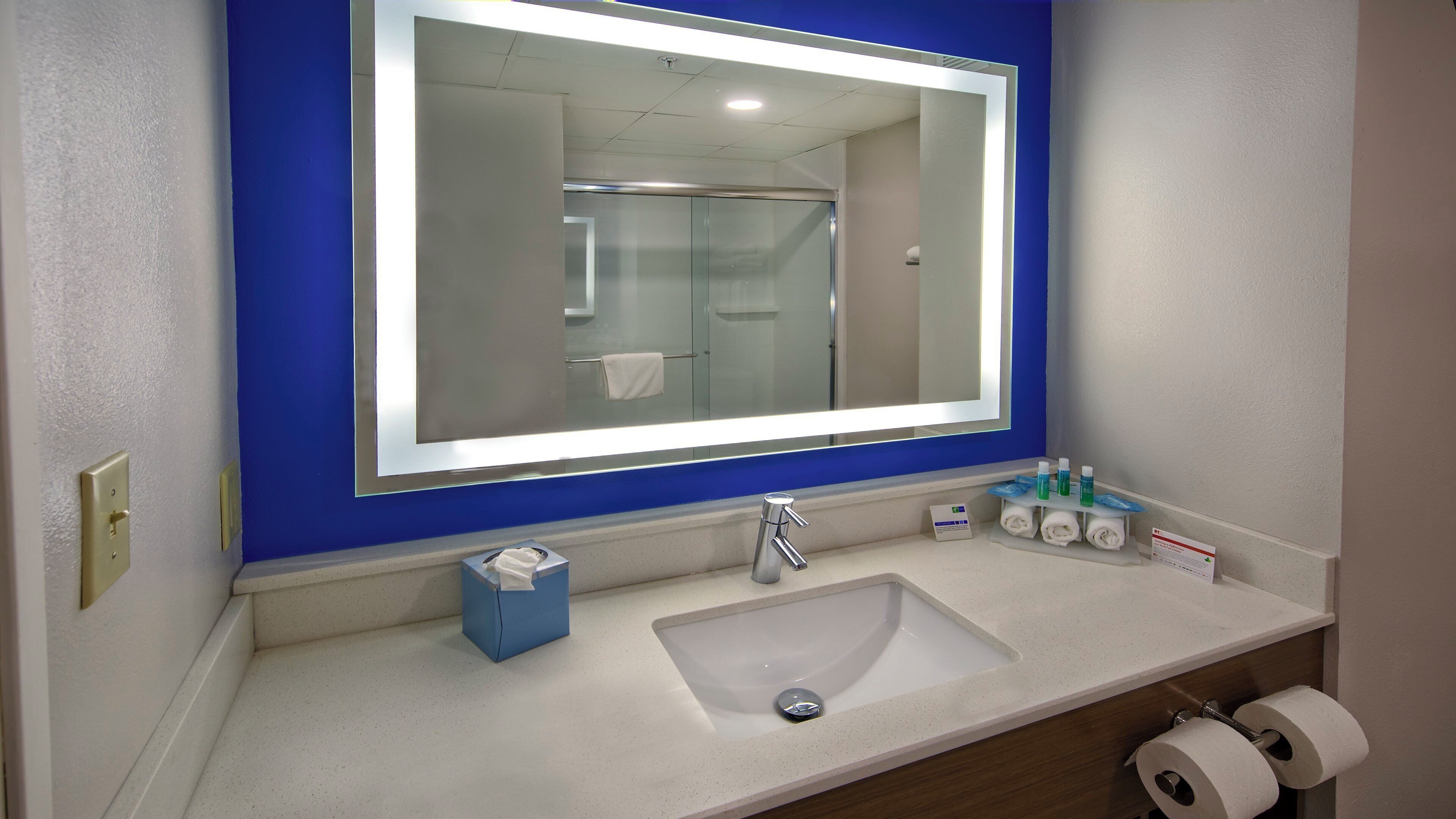 A bathroom with a large mirror, a sink, and toiletries.