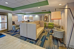 A hotel lobby with a sectional sofa, a desk with a computer, and a green armchair.