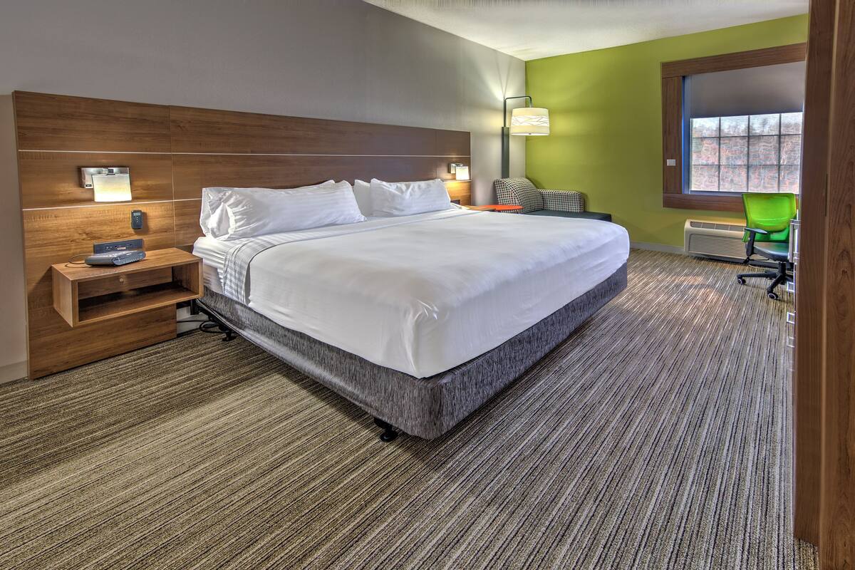 Una moderna camera d'albergo con un letto grande, una testiera in legno, un comodino con una lampada e vista all'esterno attraverso una finestra.