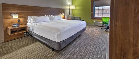 A modern hotel room with a large bed, a wooden headboard, a bedside table with a lamp, and a view of the outside through a window.