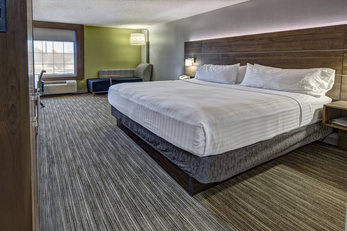 Camera d'albergo con un letto grande, una testiera in legno, un tavolino, una sedia e una finestra con vista all'esterno.