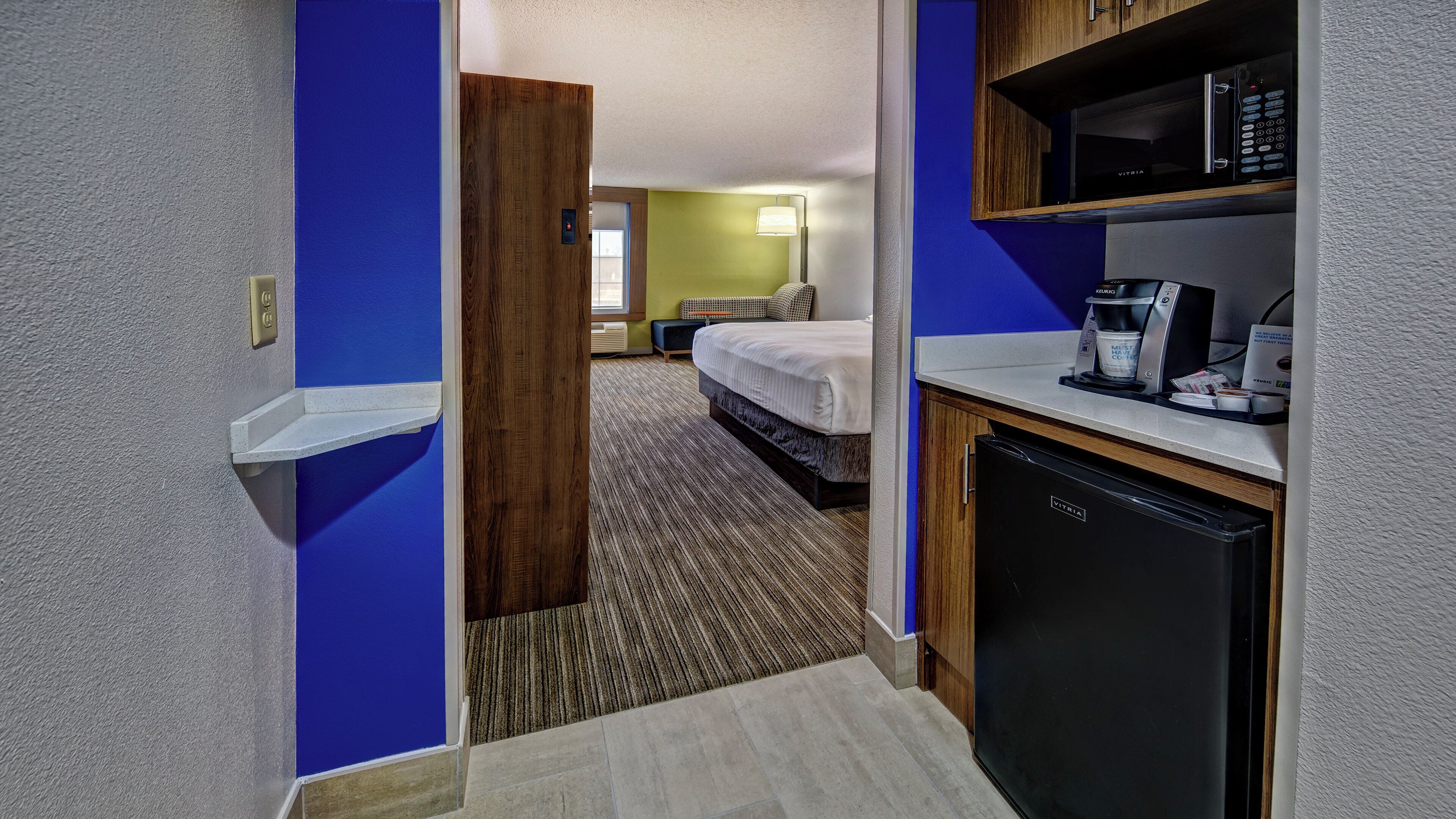 A hotel room with a kitchenette, a bed, and a bathroom.