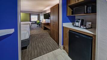 Quarto de hotel com cozinha compacta, cama, escrivaninha e televisão.