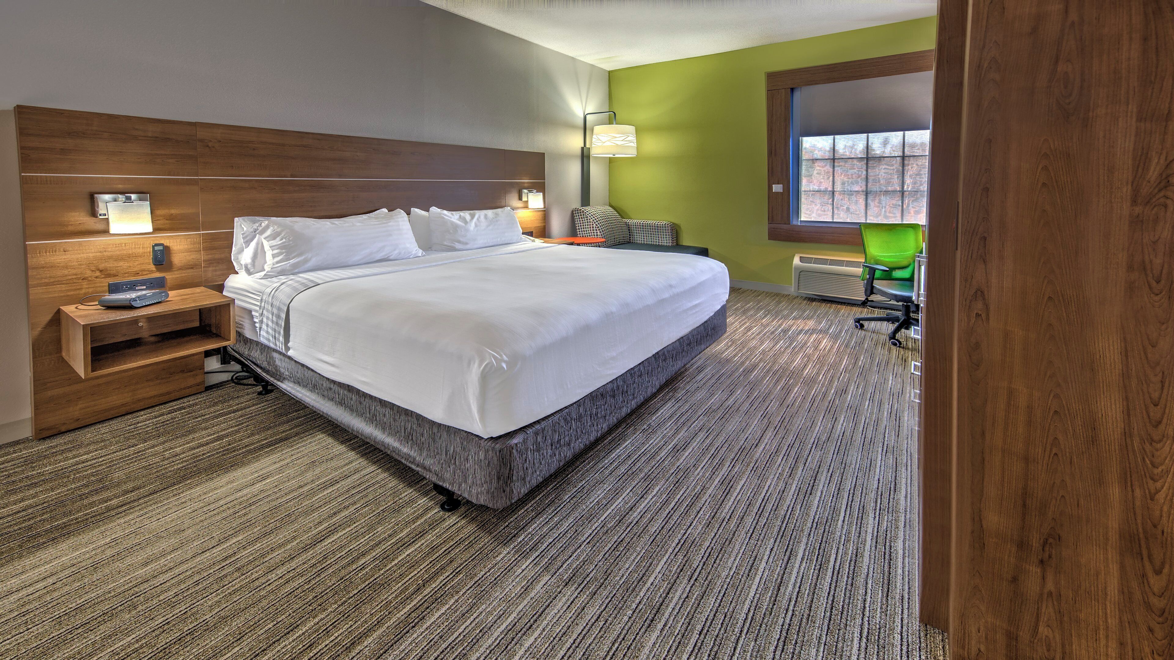 A hotel room with a large bed, bedside tables, a desk, a chair, and a window with a view.