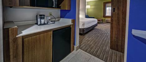 Une chambre d’hôtel de taille réduite, dotée d’une kitchenette, d’un lit et d’une petite salle de bain.