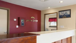 Un mostrador de recepción de madera con una pared roja detrás. Se observa una placa con el nombre "Howard Johnson" y un pequeño dispositivo electrónico en la pared.