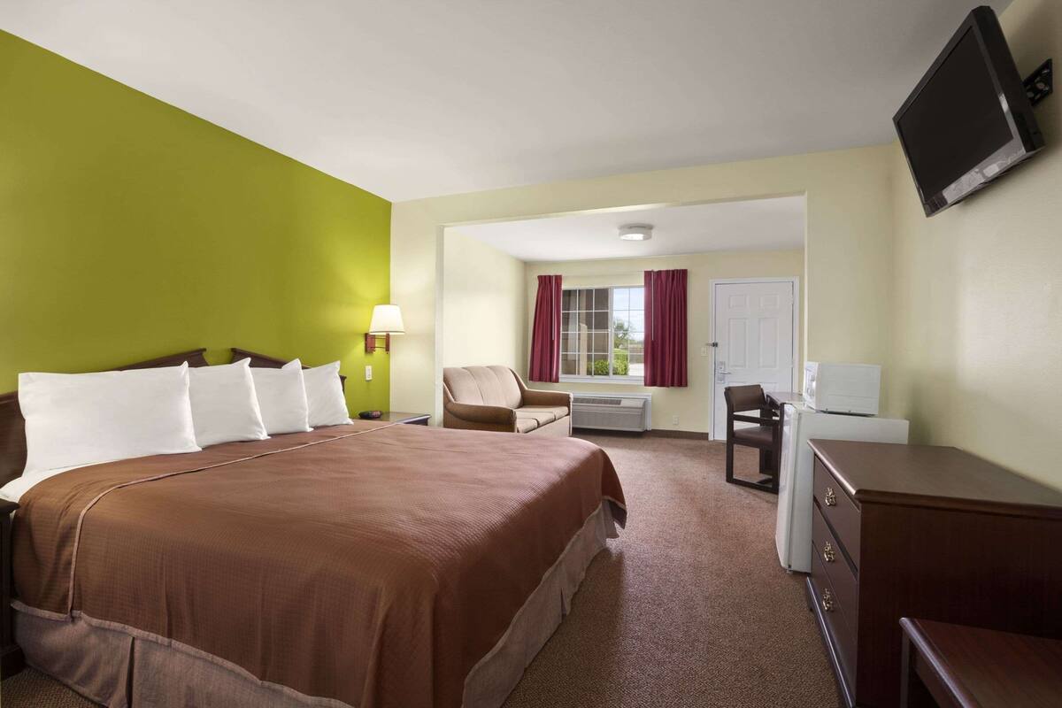 A hotel room with a large bed, a desk, a chair, a television, and a window with curtains.