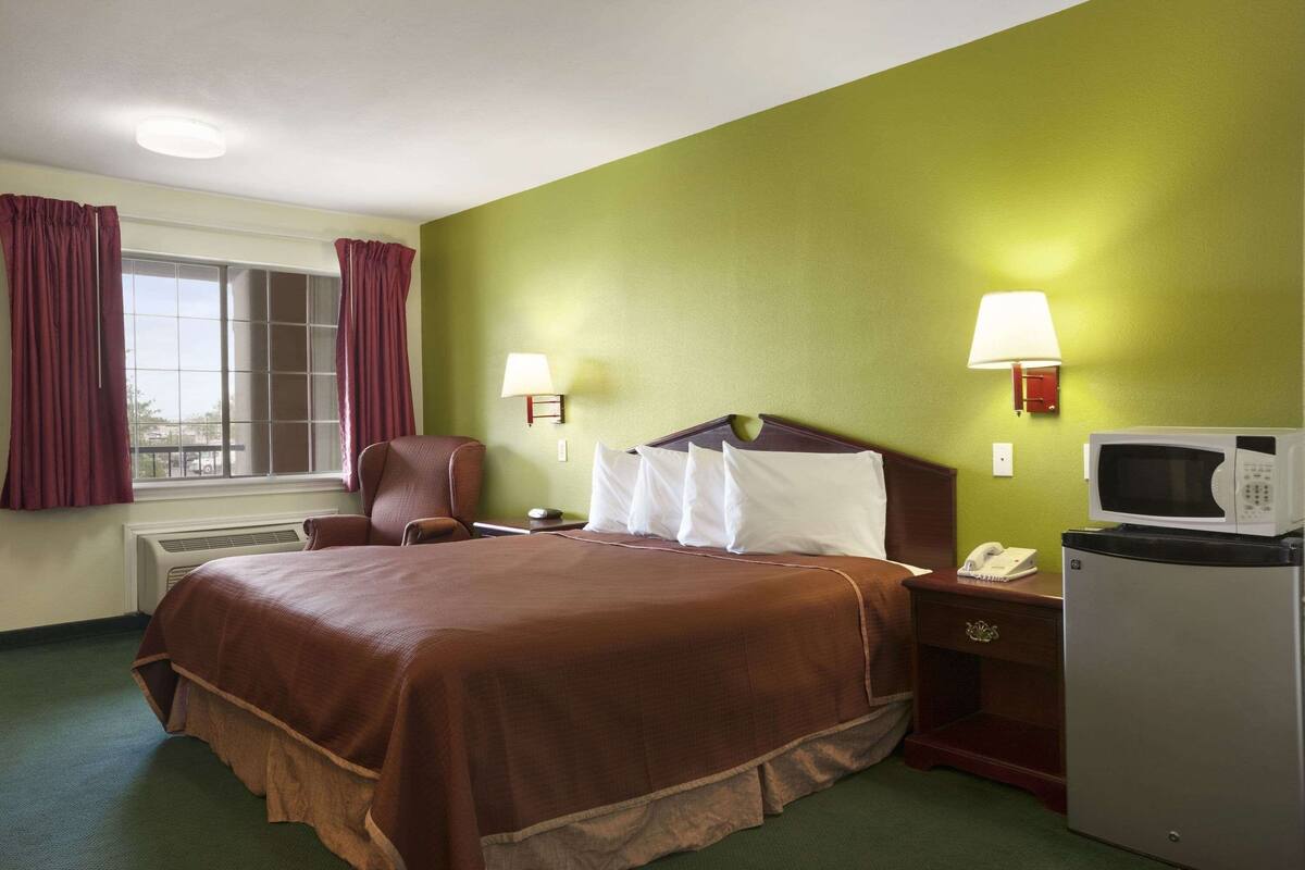 A hotel room with a large bed, two bedside lamps, a microwave, and a telephone on a nightstand.