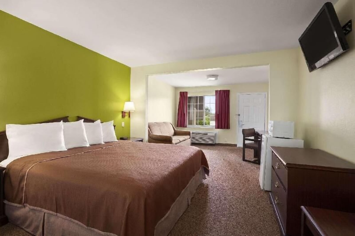 Une chambre d’hôtel avec un grand lit, un bureau, une chaise, une télévision et une fenêtre avec des rideaux.