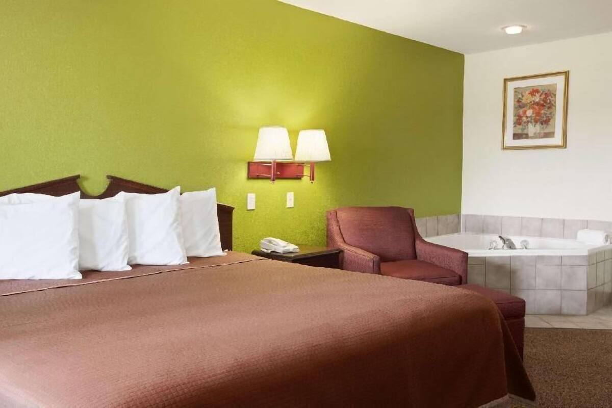 A hotel room with a bed, a chair, a desk, a telephone, and a bathtub.