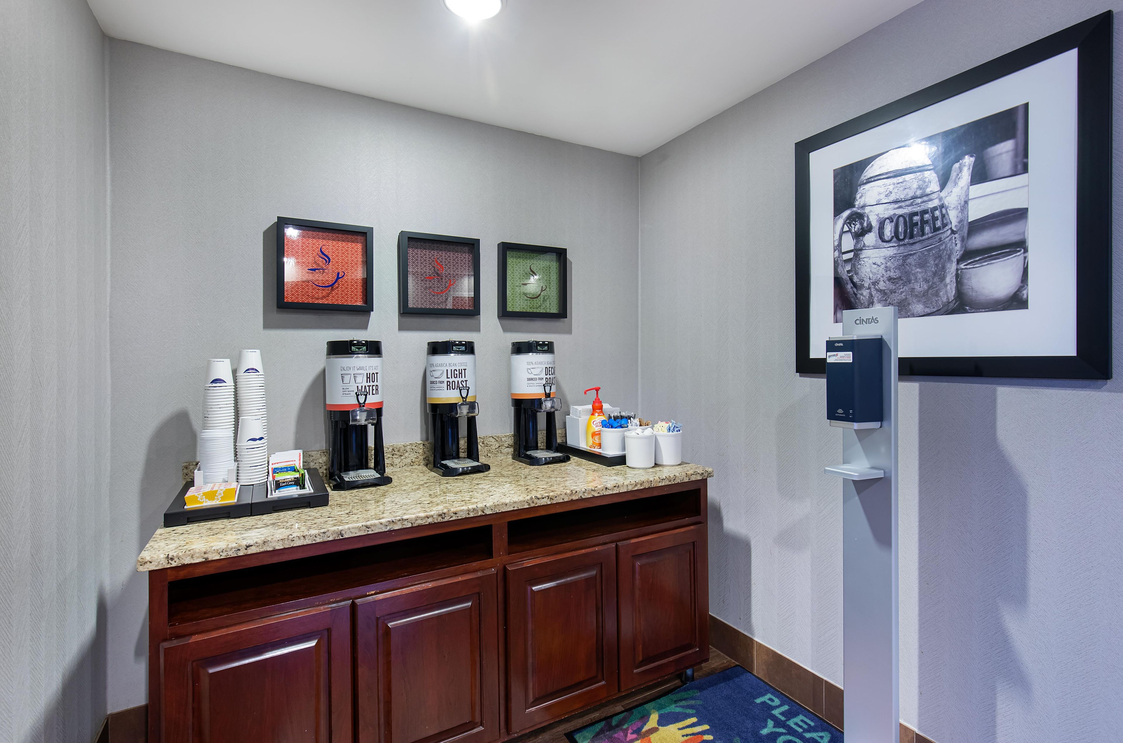 Una habitación de hotel con estación de café, cuadros en la pared y una cafetera.