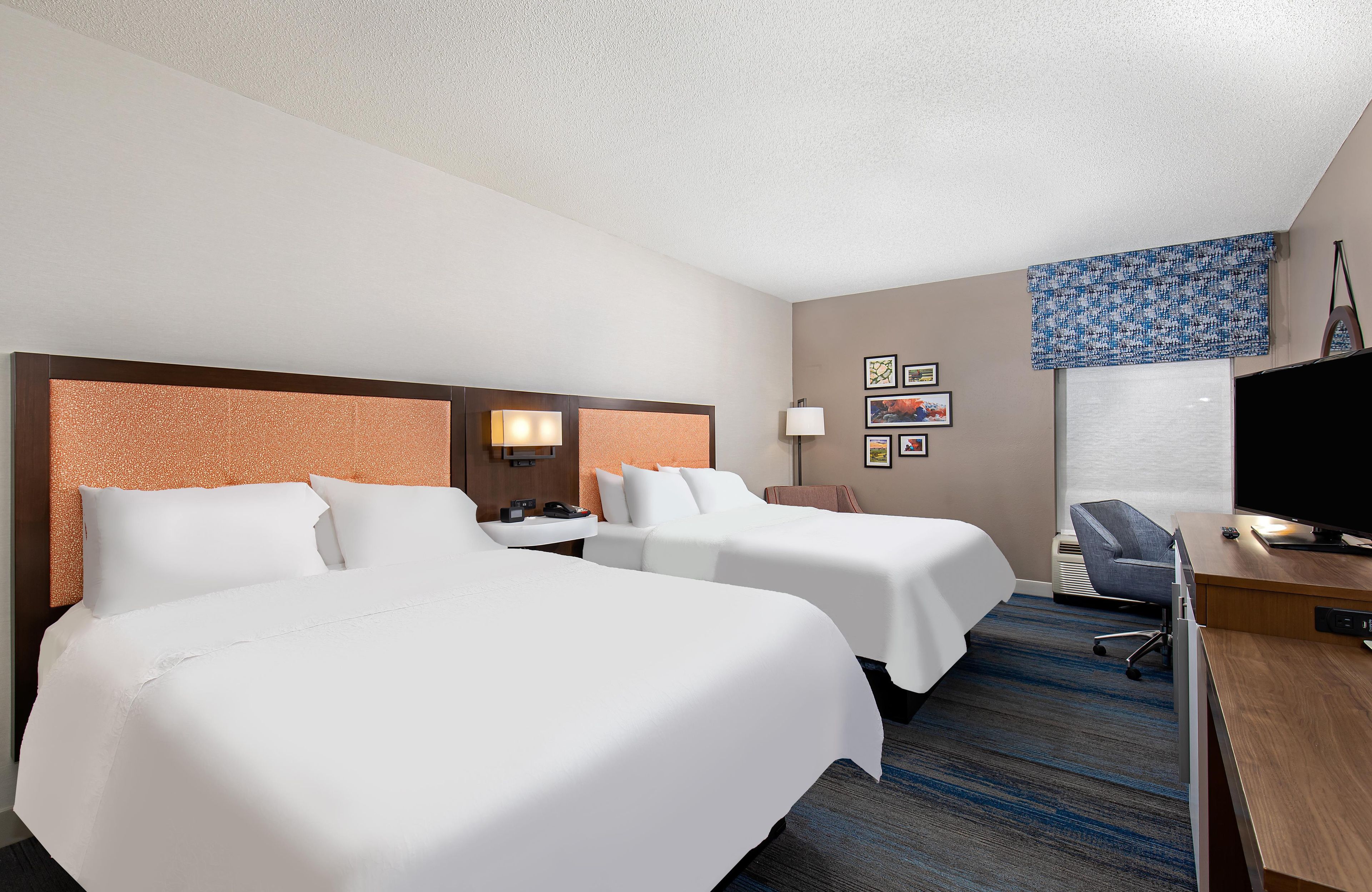 A hotel room with two beds, a desk with a computer, a TV, and a window with a view.