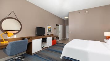 A hotel room with a bed, desk, chair, TV, and a bathroom visible in the background.