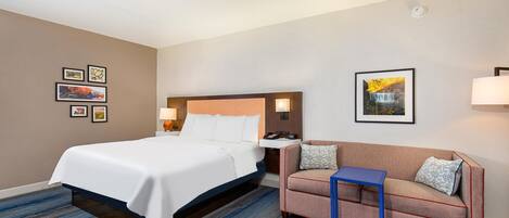 A hotel room with a bed, a sofa, a small table, and a wall-mounted lamp.