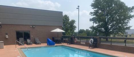 A rectangular swimming pool with a metal ladder on one side, surrounded by a brick patio.