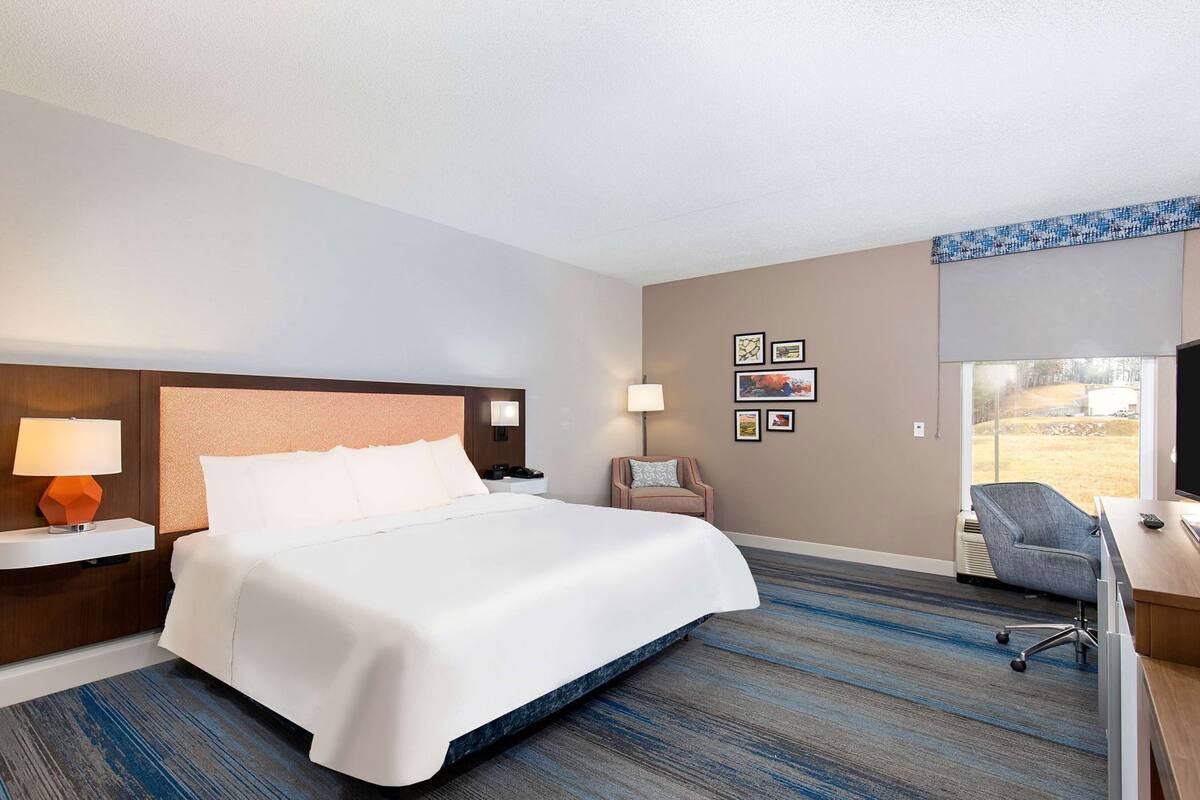A hotel room with a large bed, a desk with a chair, a TV, and artwork on the wall.